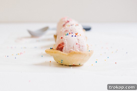 A scoop of delicious ice cream being placed into a freshly baked, sprinkle-coated cookie cup.