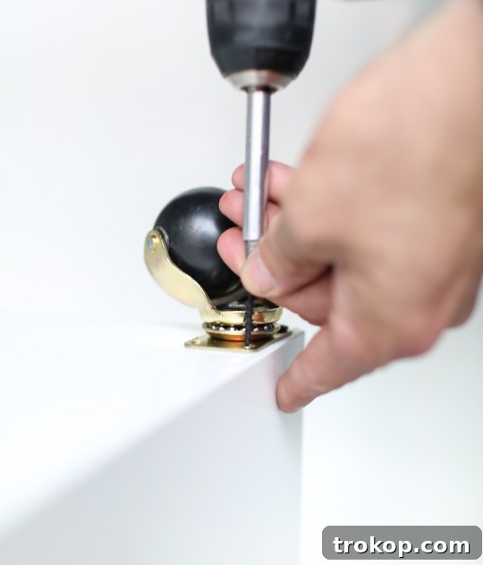 Close-up of brass casters being installed on the bottom of an Ikea Kallax shelf for a DIY bar cart hack.