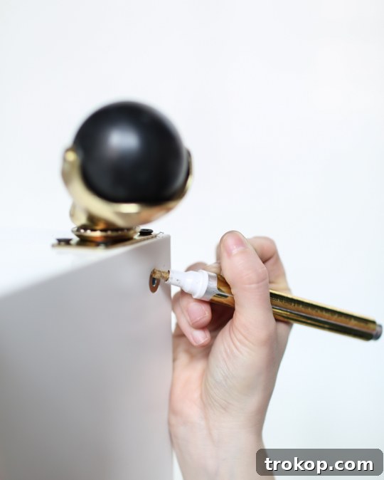 Detail of screws being colored with a gold foiling pen on the DIY Ikea bar cart hack for a unified brass look.