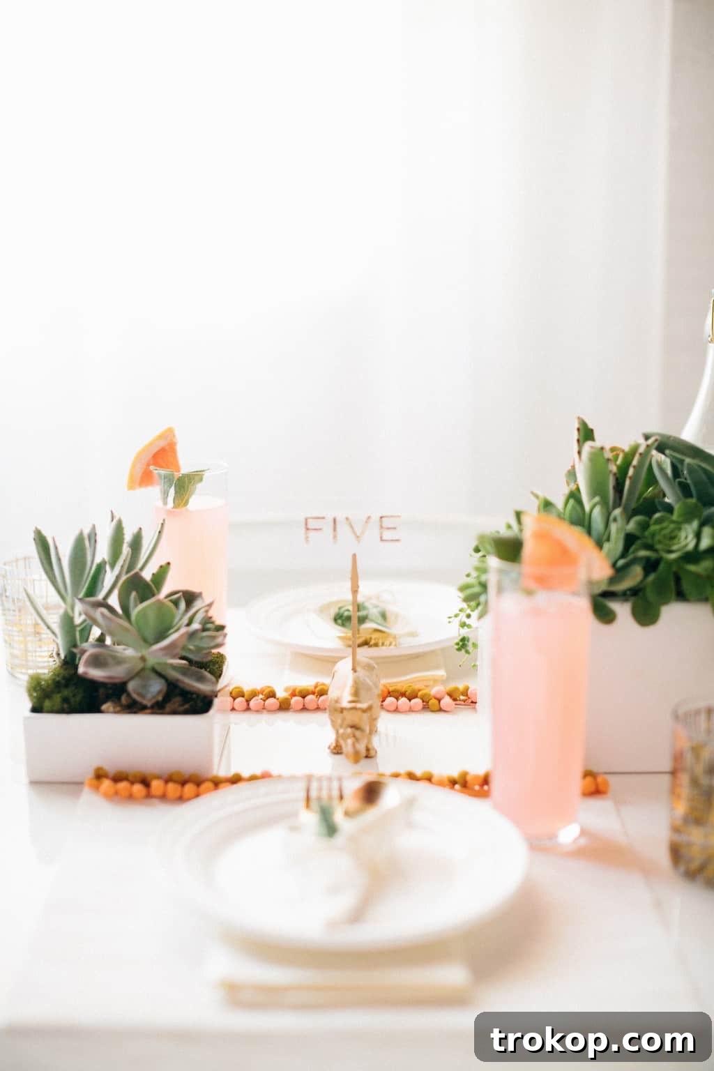 Artfully arranged table setting with DIY pom pom placemats, gold accents, and lush greenery