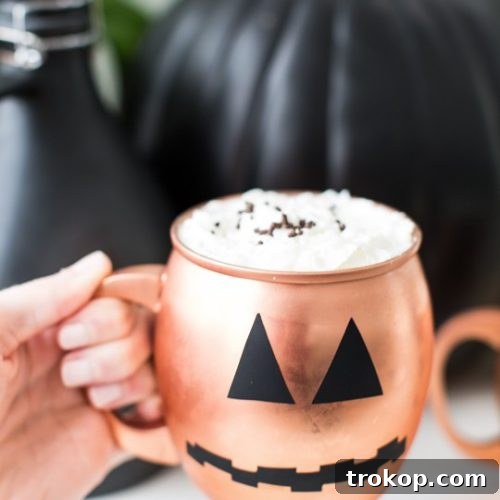 Photo of a hand holding a copper mug with a pumpkin face on it