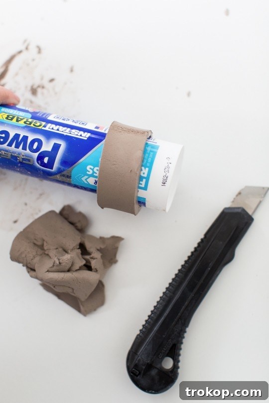 Wrapping a strip of clay around a caulk tube to form the napkin ring base