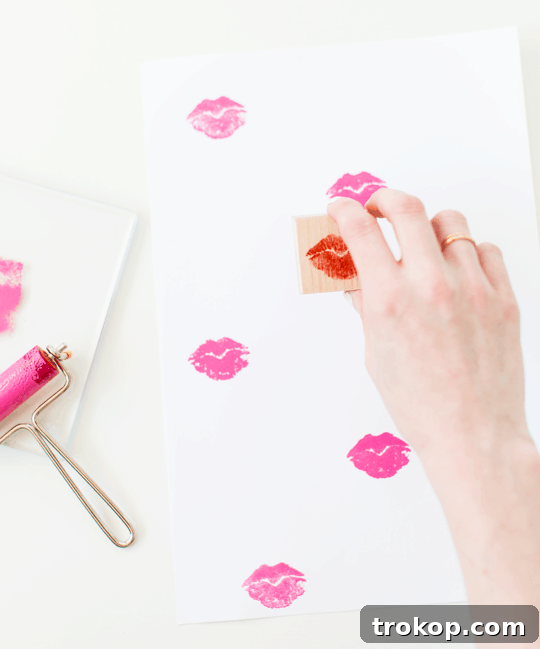 Pucker Up DIY Gift Wrap 6 A hand stamping a pink lip print onto white craft paper, showing the initial stage of pattern creation.