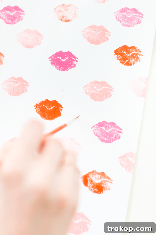 Pucker Up DIY Gift Wrap 8 A hand applying gilding adhesive with a fine brush onto the lip-patterned paper, preparing for gold leaf application.