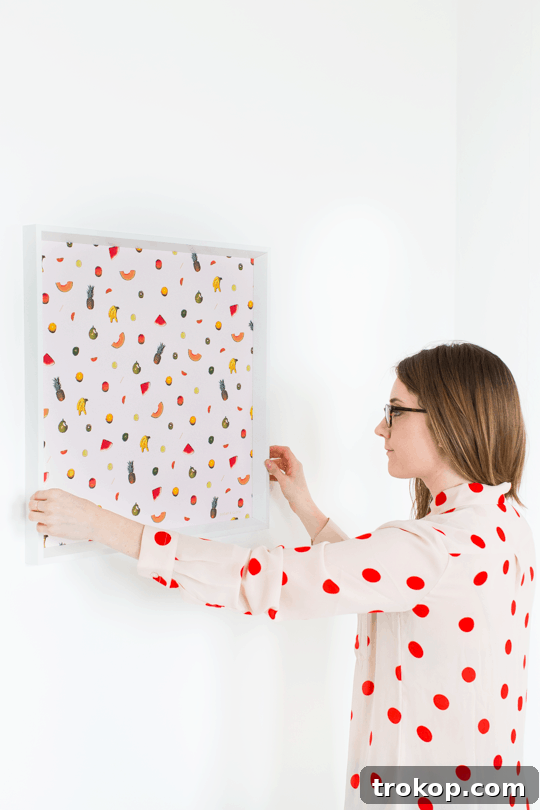 Person hanging DIY printable fruit wall art in a brightly lit studio.