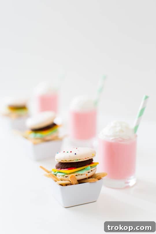 A vibrant display of miniature macaron cheeseburgers, cookie fries, and a tiny pink milkshake, artfully arranged on a serving tray.