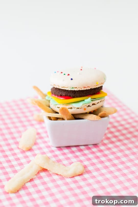 Close-up shot of the mini macaron cheeseburgers, showcasing the detailed layers of cookie patty, fondant cheese, and lettuce, alongside crisp cookie fries.