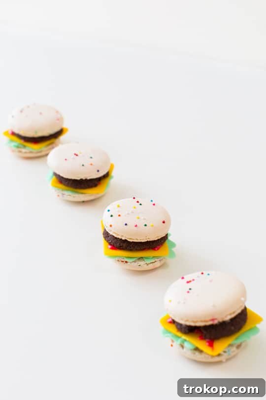 A partially assembled macaron cheeseburger, showing the layers of macaron bun, chocolate cookie patty, and red icing.