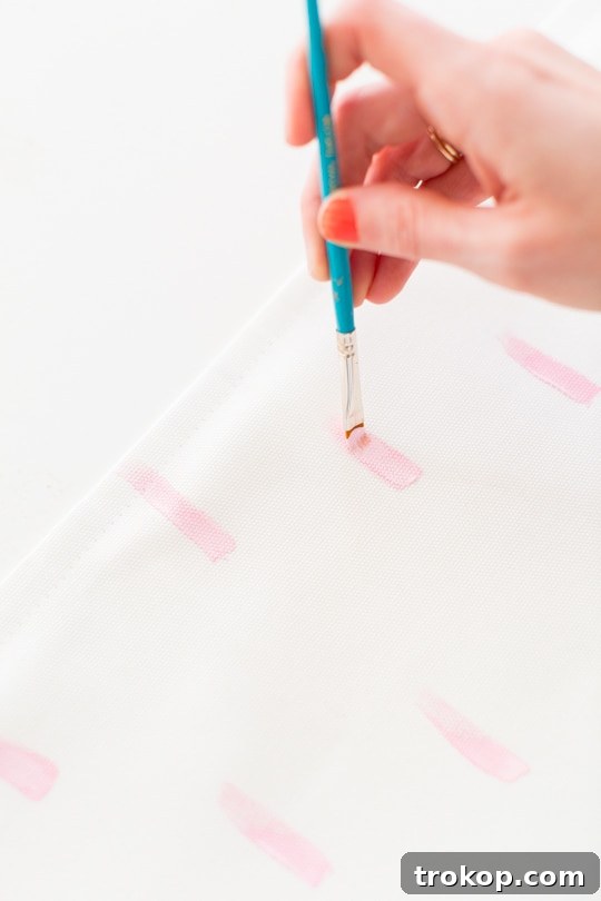 Hand carefully painting a pattern onto a white throw pillow cover