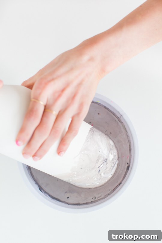 A hand dipping a white ceramic vase into swirled nail polish and water, creating a marble effect.