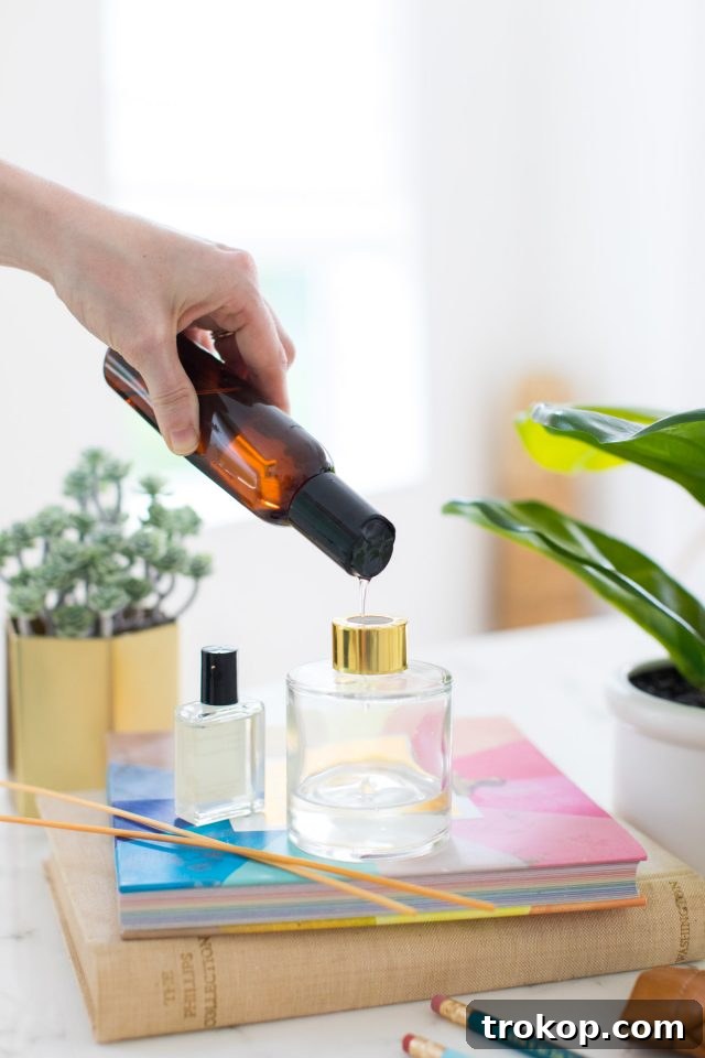 Handcrafted Home Fragrance 5 Hands carefully pouring essential oils into a clear diffuser bottle using a funnel, a key step in making a DIY reed diffuser.