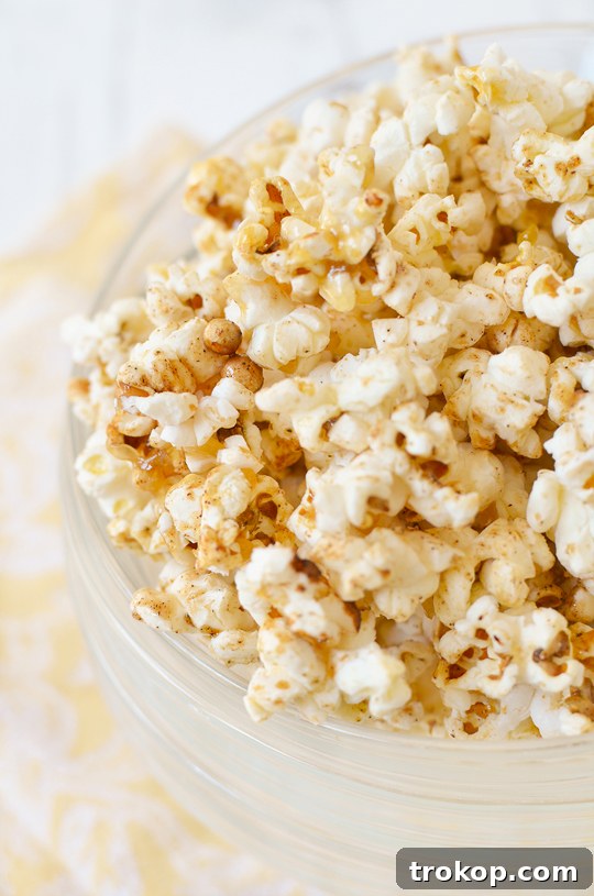 A large bowl of homemade Pumpkin Pie Kettle Corn sits on a rustic wooden surface, surrounded by fall decor.