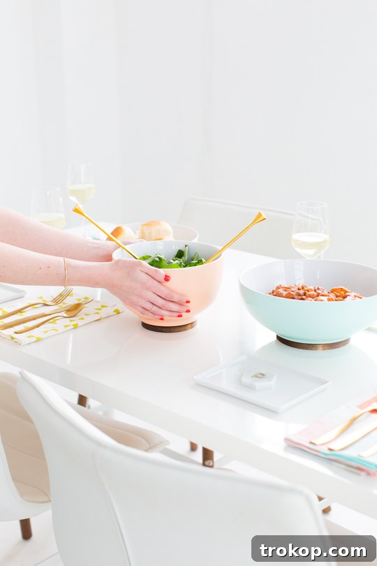 A beautifully set table featuring a DIY Footed Serving Bowl filled with fresh salad, surrounded by wine glasses and other dinnerware.