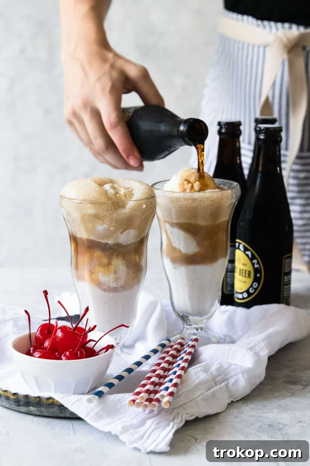 Root beer soda being slowly poured into a glass already containing scoops of vanilla ice cream, creating a frothy effect.