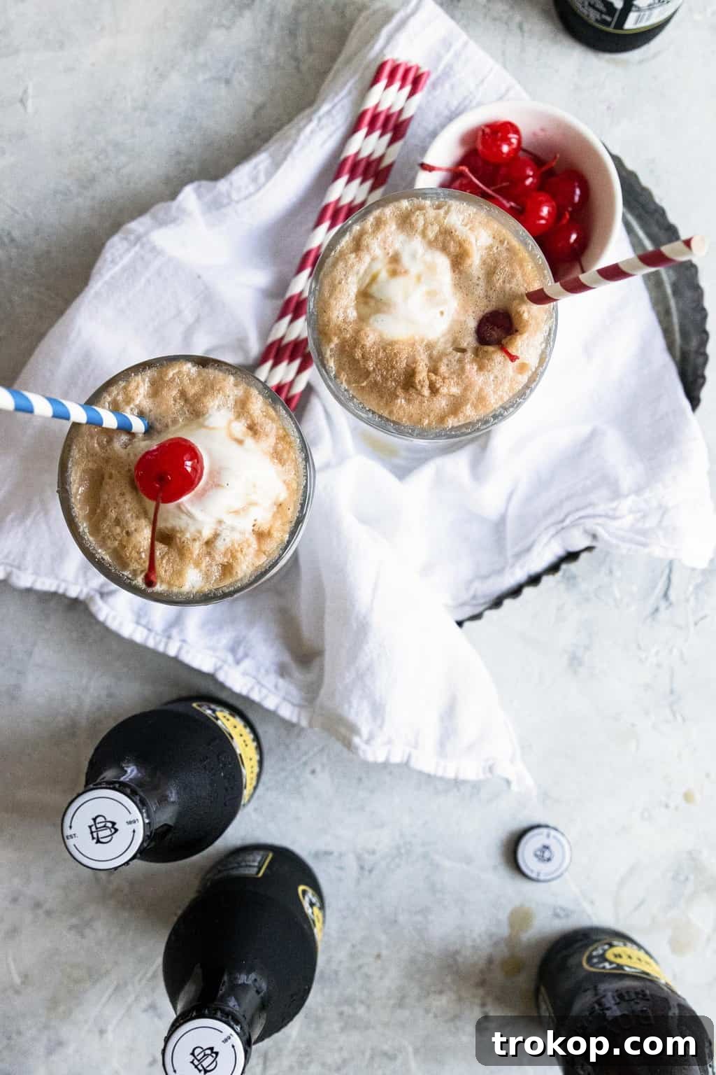A classic root beer float with a bright red maraschino cherry on top, sitting on a wooden surface.