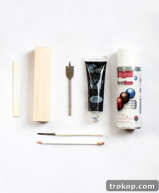 Handmade Patterned Candle Decor 4 A collection of materials and tools laid out on a clean surface, including a block of wood, spray paint, acrylic paint, a paintbrush, and a drill, ready for crafting a DIY wooden candle holder.