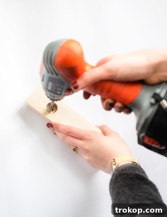 Handmade Patterned Candle Decor 5 A hand carefully drilling into a block of wood with a hand drill, creating recesses for candles to sit, demonstrating a key step in making a DIY wooden candle holder.