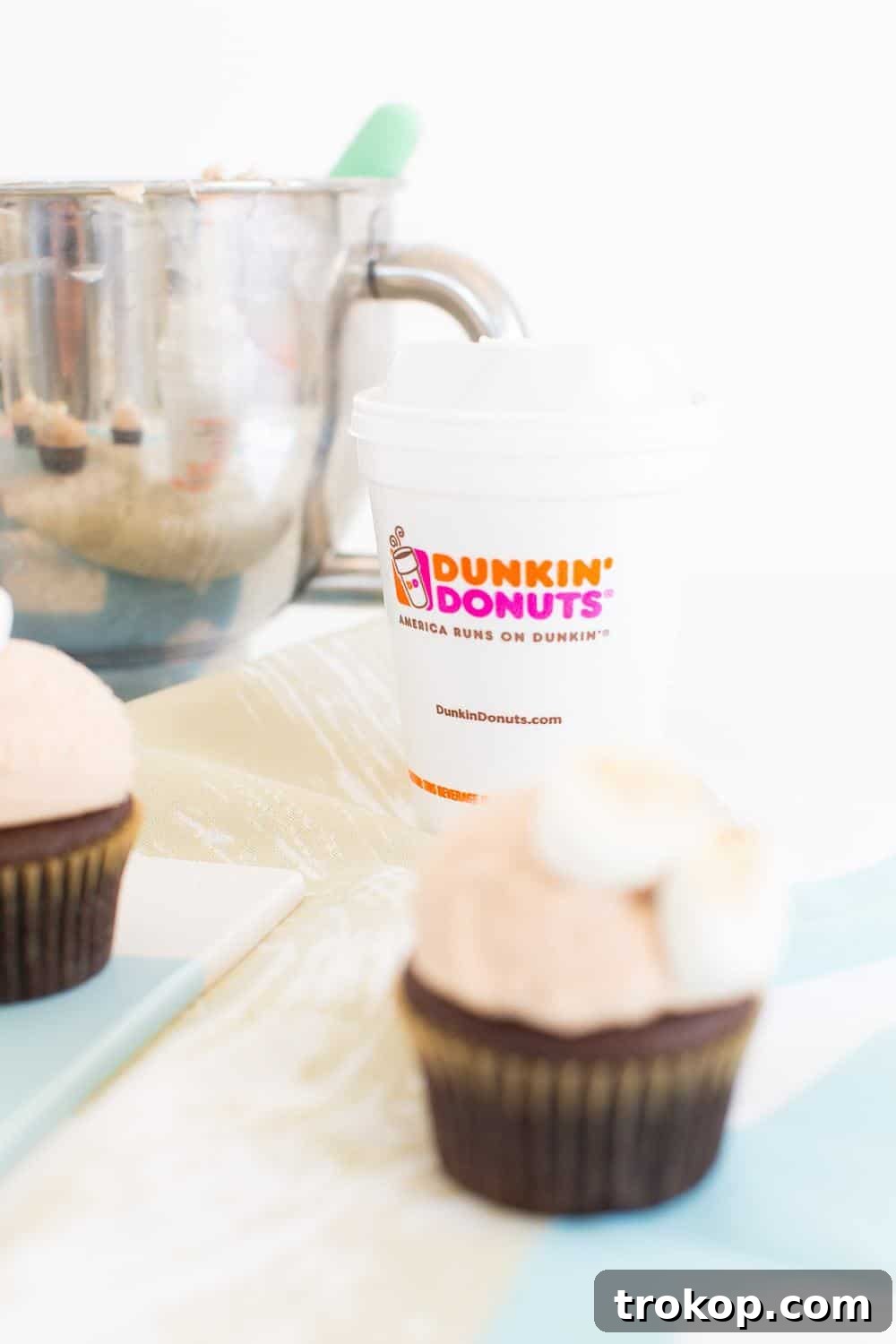 A finished cupcake with a generous scoop of Dunkin' Donuts hot chocolate frosting, ready for topping.