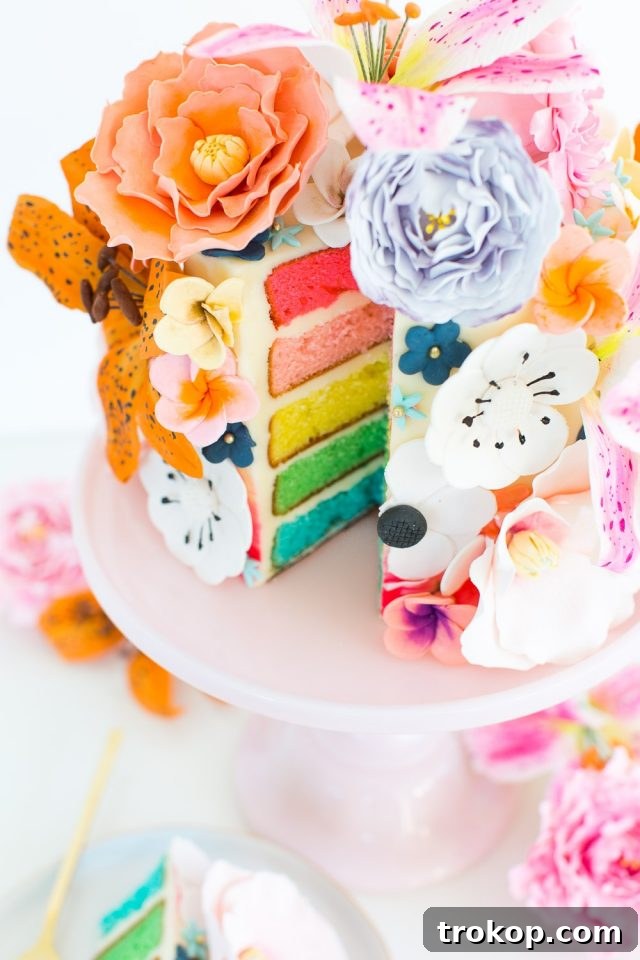A slice of vibrant rainbow cake with colorful layers, ready to be decorated with sugar flowers.