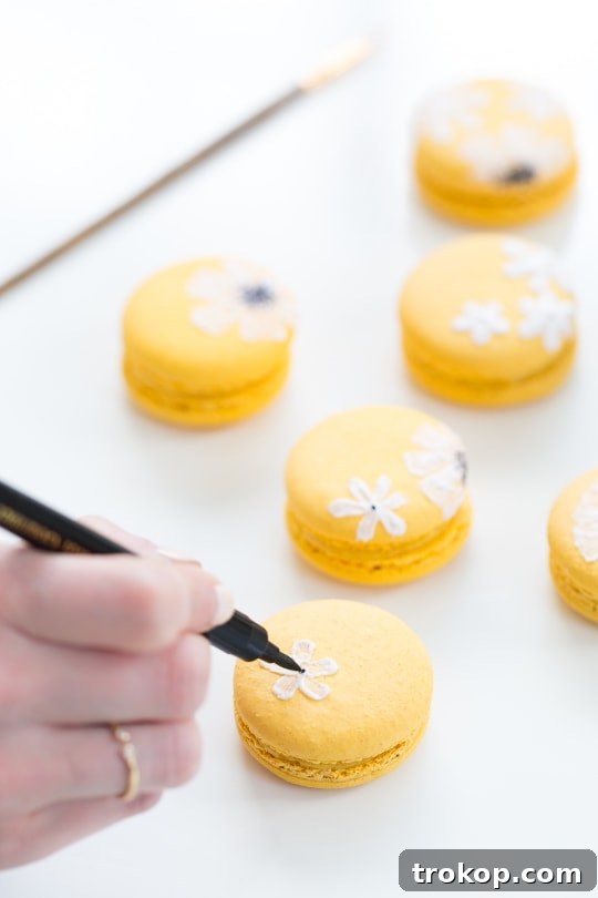Painting white royal icing petals onto a yellow macaron shell