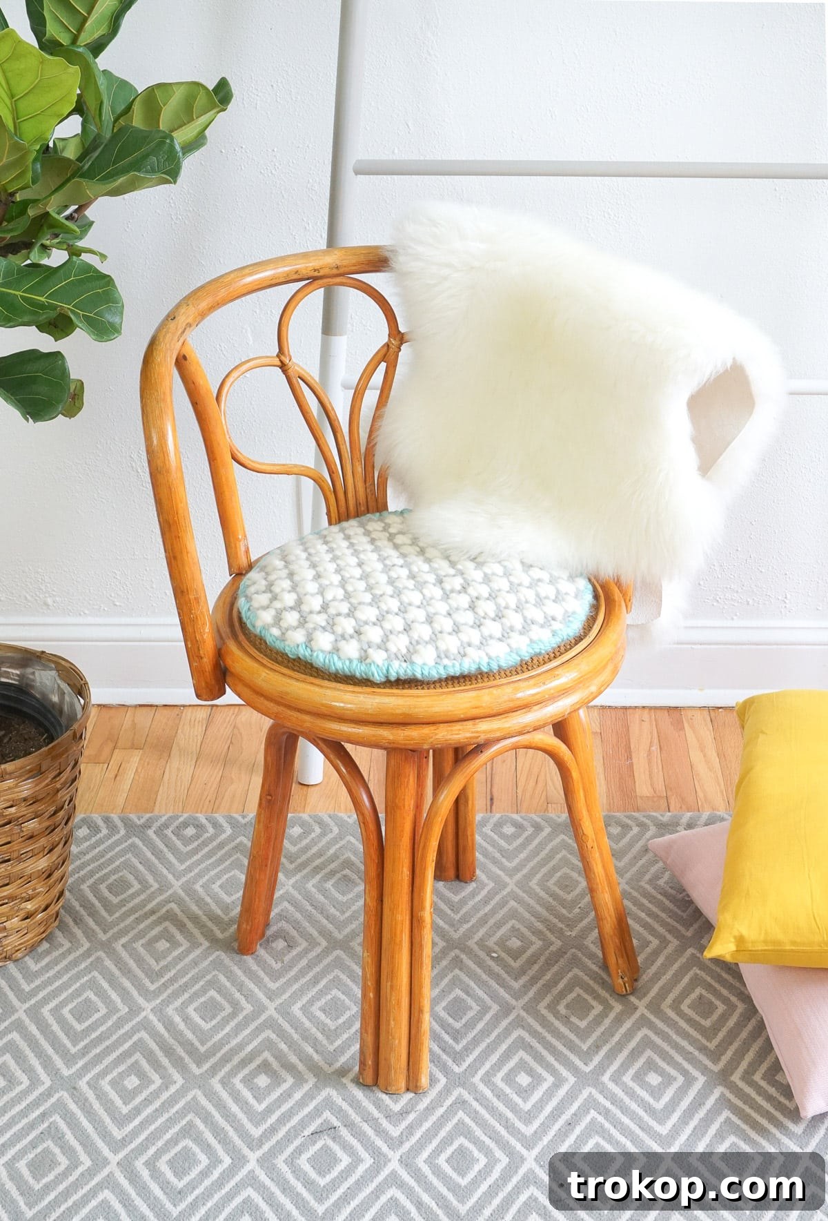 Artisan Oversized Cross-Stitch Pillow 2 A vibrant, oversized cross-stitched cushion featuring a bold pattern, resting on a stylish mid-century rattan chair, enhancing the home decor with rich texture.