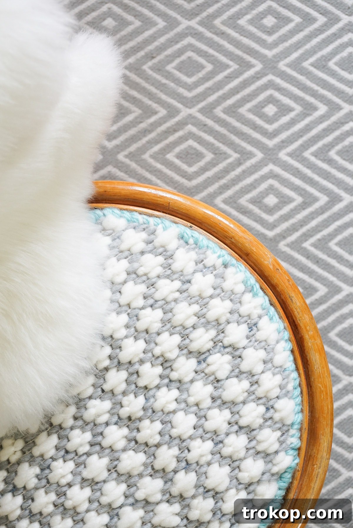 Artisan Oversized Cross-Stitch Pillow 3 Close-up of the textured, oversized cross-stitch pattern on the cushion, showcasing the chunky yarn and its modern appeal against a rattan chair.