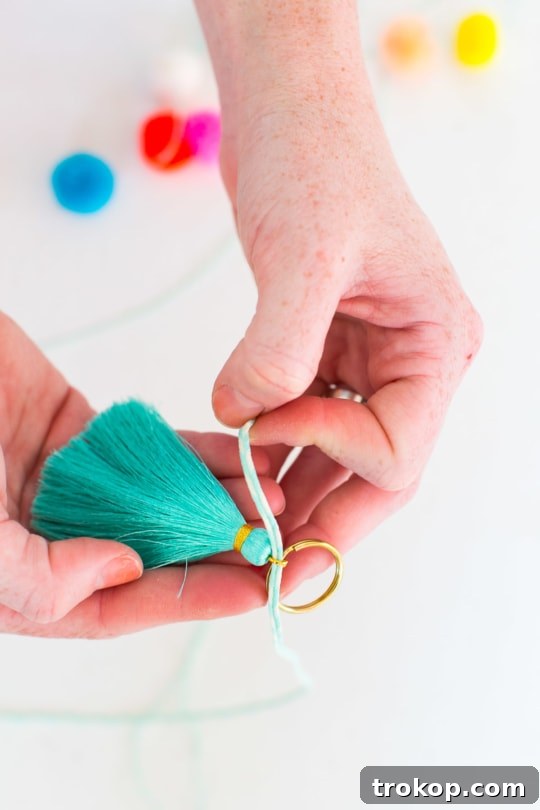 Securing the tassel strand to a gold keyring, reinforcing the knot for durability.
