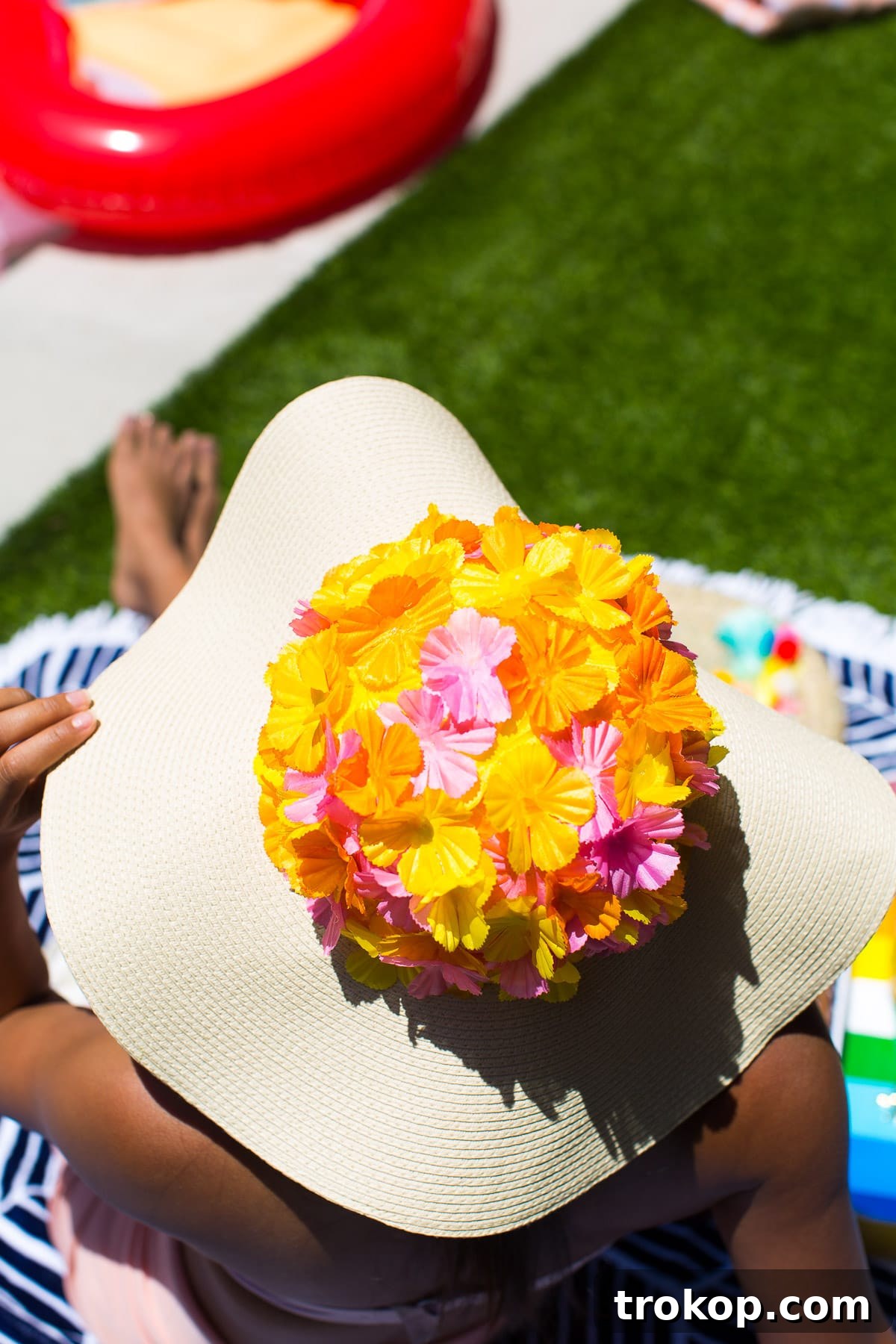 Hands meticulously gluing faux flowers onto the dome of a floppy hat, demonstrating the DIY process.