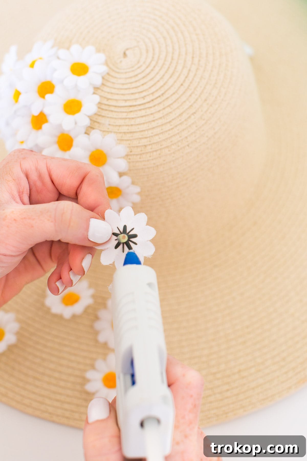 Close-up view of faux flowers being glued onto a floppy hat, showing the overlapping technique for a full look.