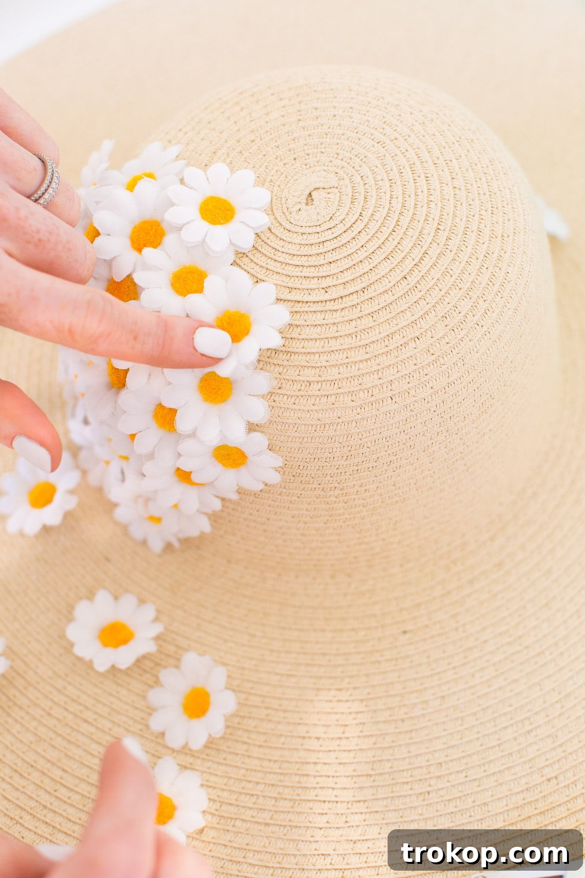 The process of attaching faux flowers to a floppy hat continues, ensuring thorough coverage of the dome.