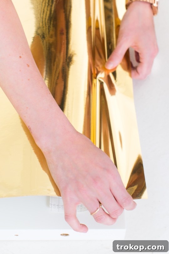 DIY Faux Brass Headboard: Get the High-End Look for Less 4 Close-up of the metallic gold adhesive vinyl roll and tools needed for the DIY headboard project