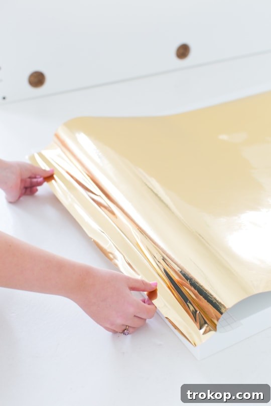 DIY Faux Brass Headboard: Get the High-End Look for Less 5 Detail shot of smoothing metallic gold vinyl onto a headboard with a craft squeegee