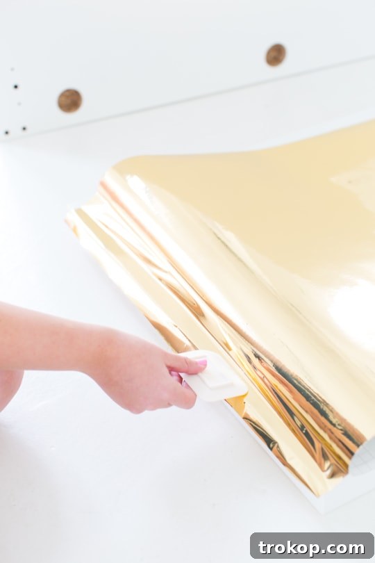 DIY Faux Brass Headboard: Get the High-End Look for Less 6 Applying metallic gold adhesive vinyl to a headboard, showing the gradual peeling and smoothing process