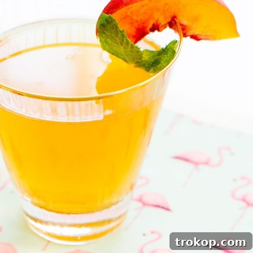 A refreshing Peachy-Tini cocktail in a martini glass with a peach slice and mint garnish