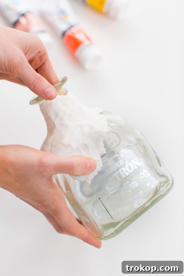 Applying air-dry clay to the neck of a glass bottle, showing careful shaping and smoothing to achieve an even coating.