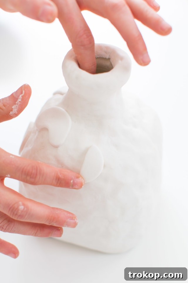 Detailed application of small, decorative clay shapes around the body of the decanter, demonstrating how to add artistic embellishments.