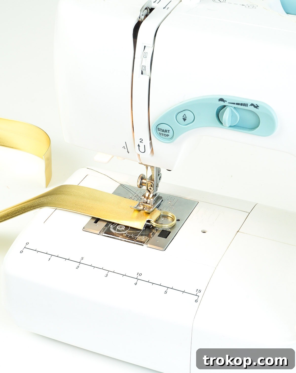 Sewing a horizontal line across the bottom of the DIY camera strap end, securing the folded flap and enclosed split ring with gold thread.