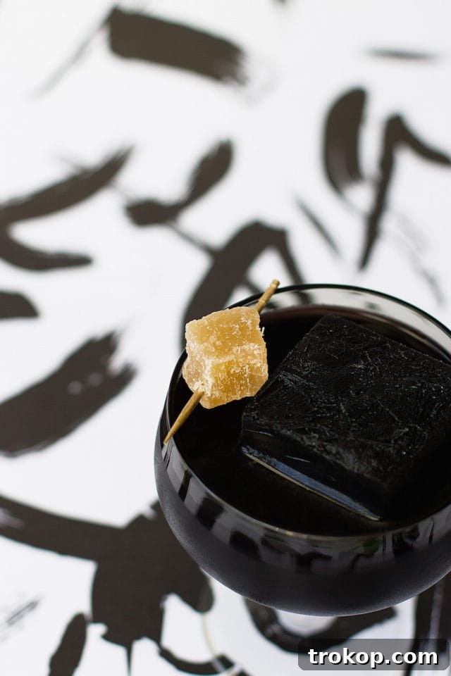 Activated Charcoal Elixirs: Detox Cocktails and Mocktails 3 Close-up of a dark activated charcoal drink garnished with fresh ginger slices, highlighting its detox and soothing properties.