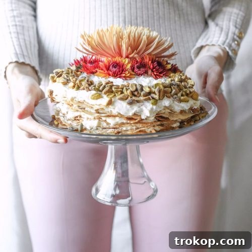 vertical photo of a girl holding a chai crepe cake on a cake stand by sugar and cloth