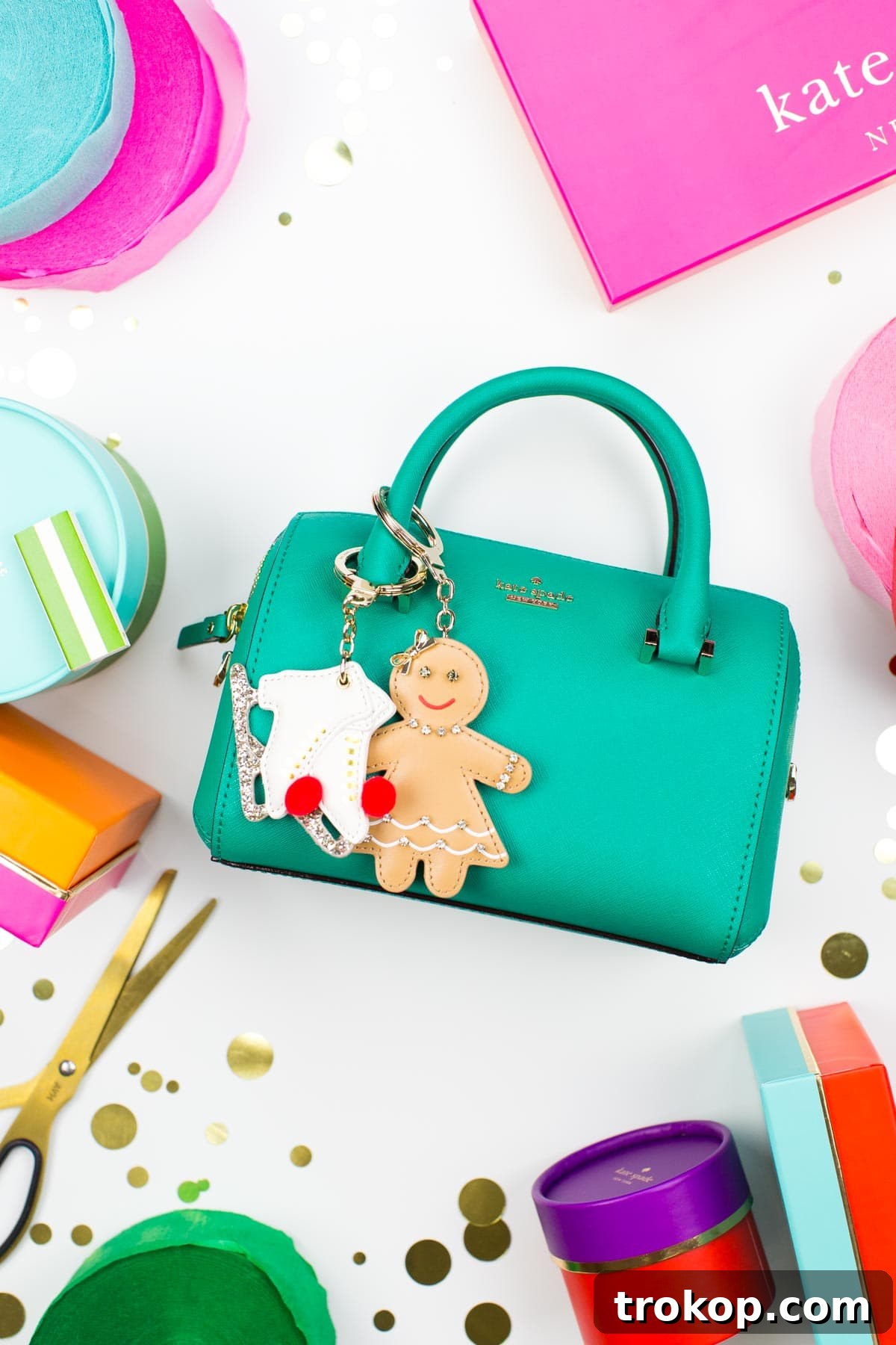 A red Kate Spade handbag adorned with festive charms and a personalized tag, surrounded by snowy decorations.
