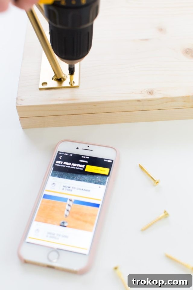 Securing the modern gold hairpin legs to the benchtop using a drill and wood screws, completing the structural assembly.