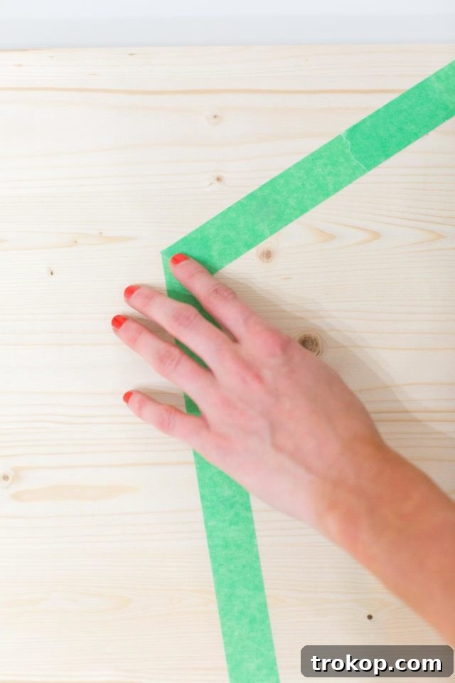 Applying painter's tape to create a bold, abstract pattern for the DIY modern low bench, preparing for painting and staining.