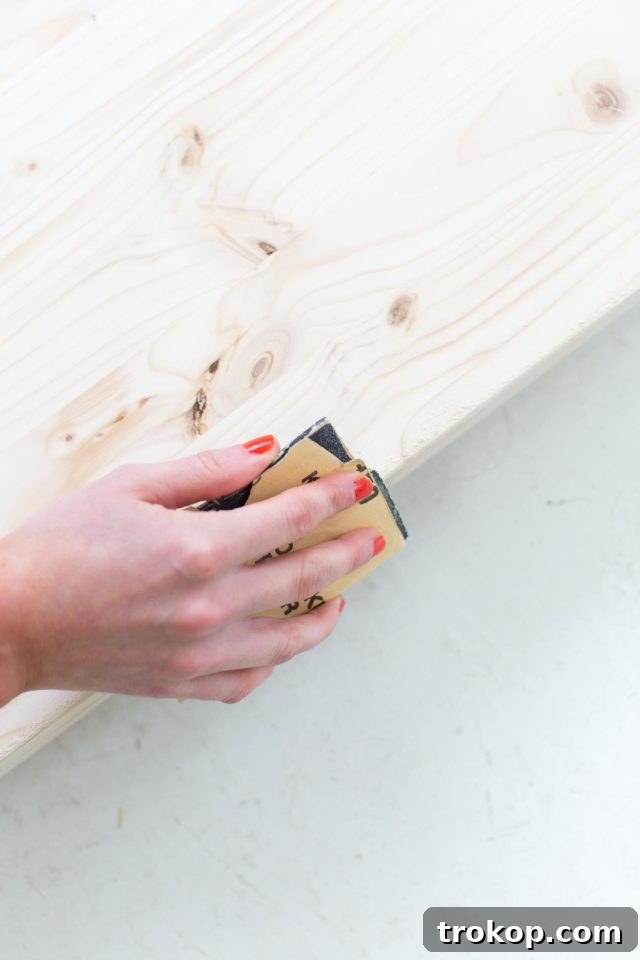 Sanding the edges of the glued wood boards for the modern low bench, ensuring a smooth and even surface.