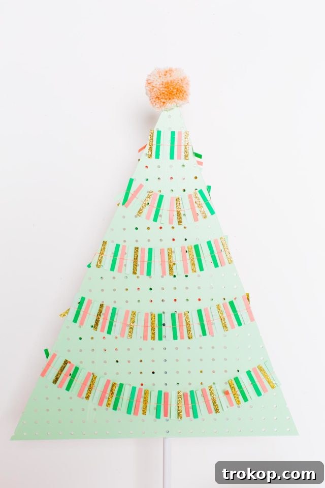 Craft a Modern Pegboard Christmas Tree 8 A minimalist DIY Pegboard Christmas tree in mint green, topped with a single pink pom-pom, styled beside a modern pink armchair.