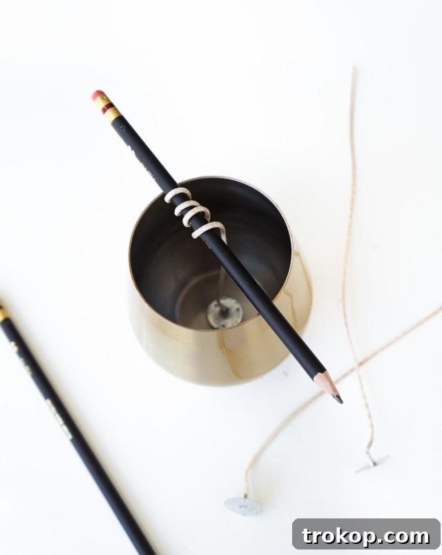 A close-up of a candle wick being secured and centered with a pencil in a container.