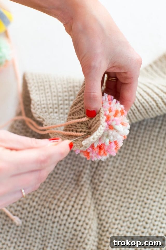 Detailed shot of pom poms being glued onto a scarf during the DIY process.
