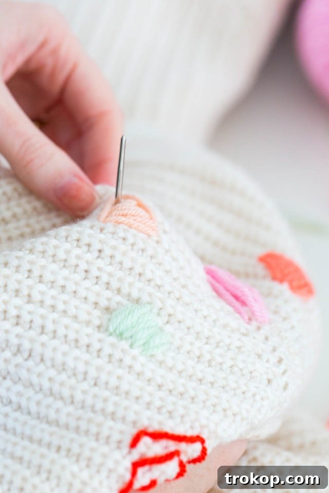 Custom Abstract Embroidery Pullover 6 Detailed shot of hands actively embroidering a sweater with colorful yarn, demonstrating the technique for creating abstract patterns and filling in shapes.