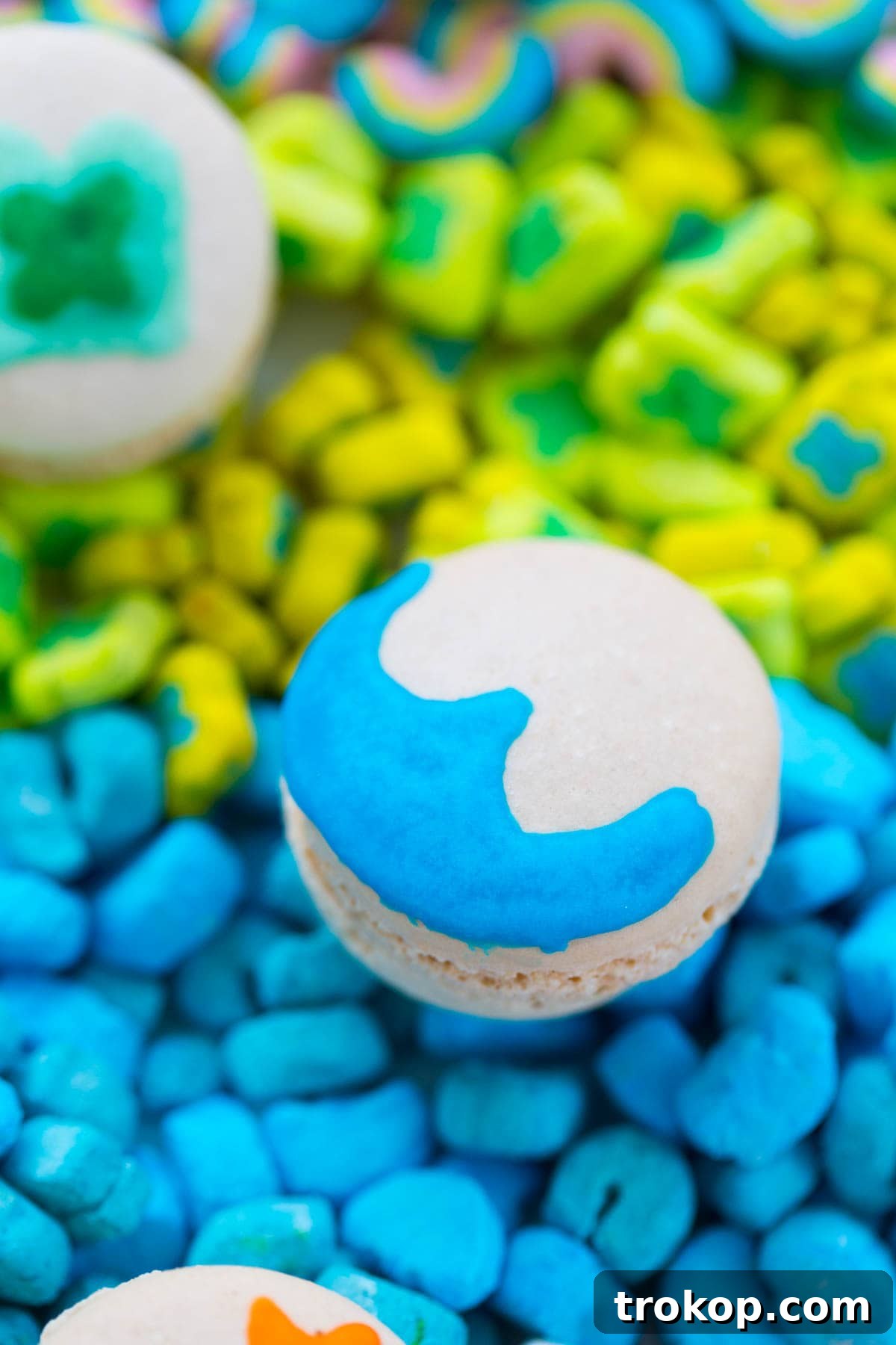 A close-up view of a partially decorated Lucky Charms Macaron shell, showcasing the detailed painting process with royal icing.