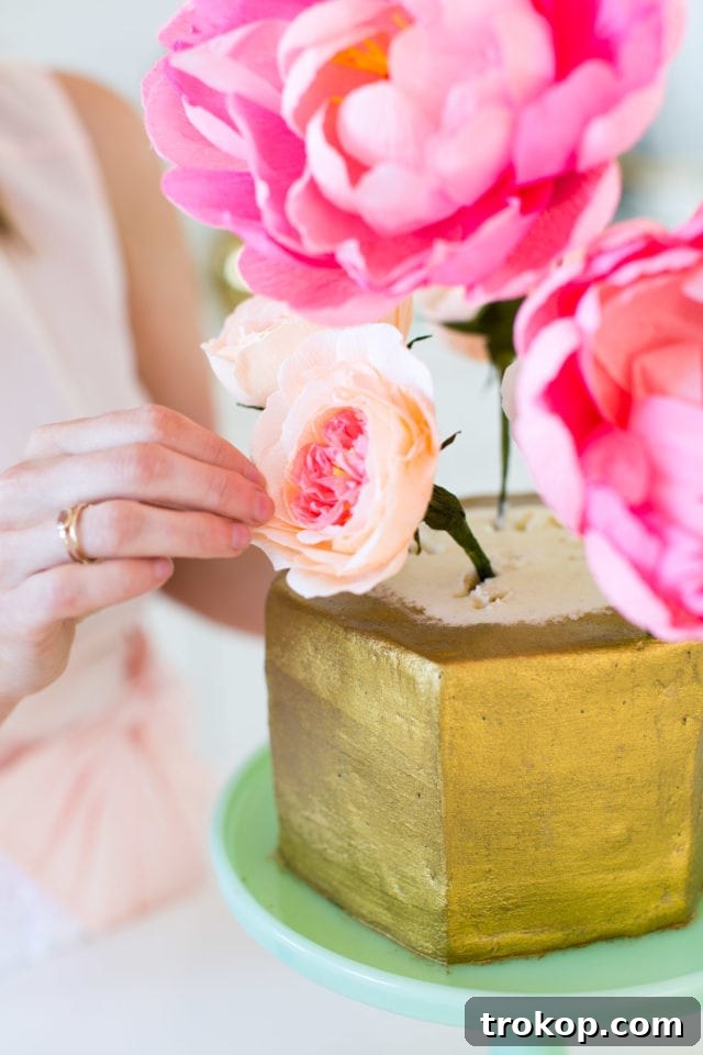 Sweet Flower Pot Cake Secrets 8 Crepe paper flowers being artfully arranged and inserted into the top of the gold-painted cake, creating a beautiful floral bouquet effect.