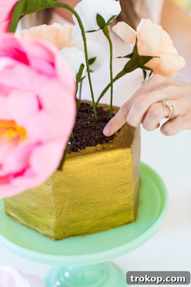 Sweet Flower Pot Cake Secrets 9 Crushed chocolate wafer cookies being generously sprinkled over the top of the cake, forming a realistic 'soil' layer around the crepe paper flowers.